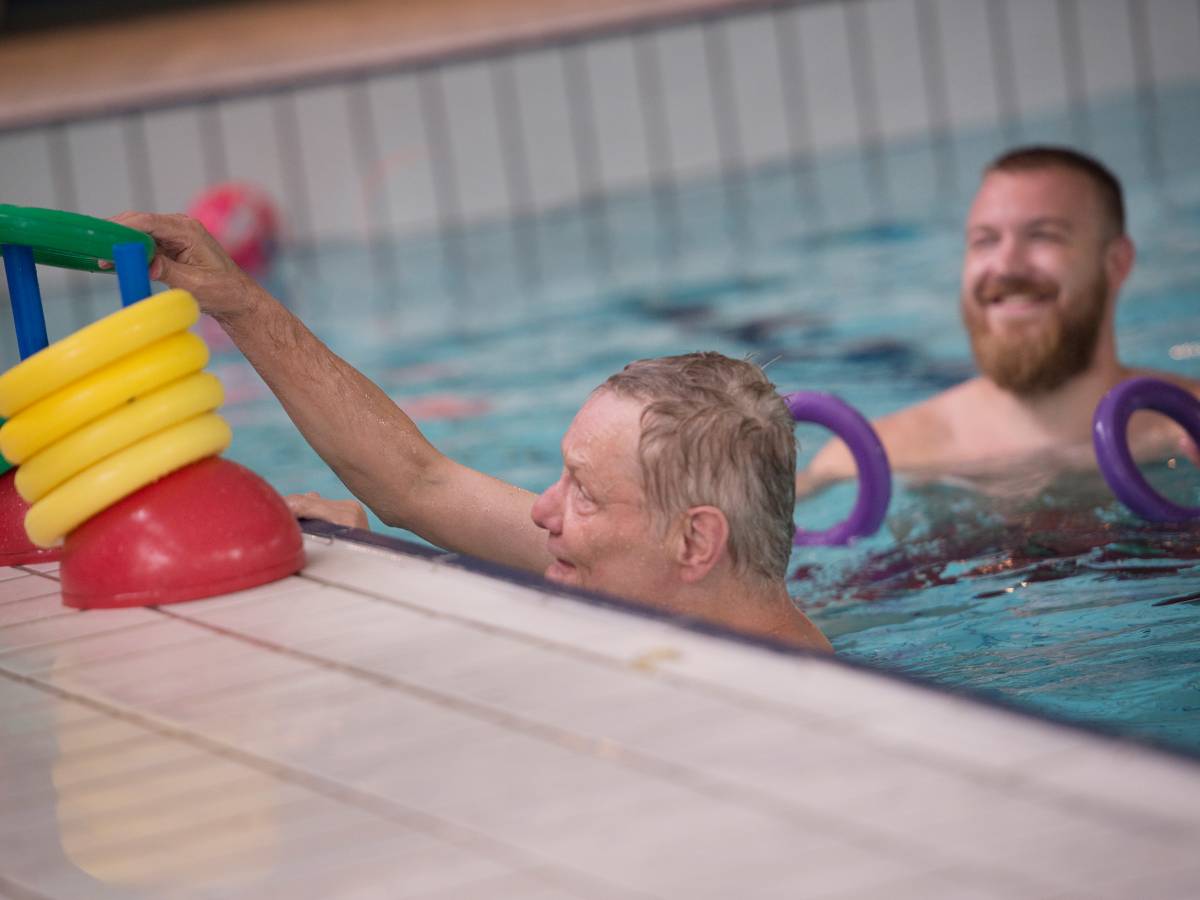 Begeleider en cliënt in zwembad activiteit met gele ringen