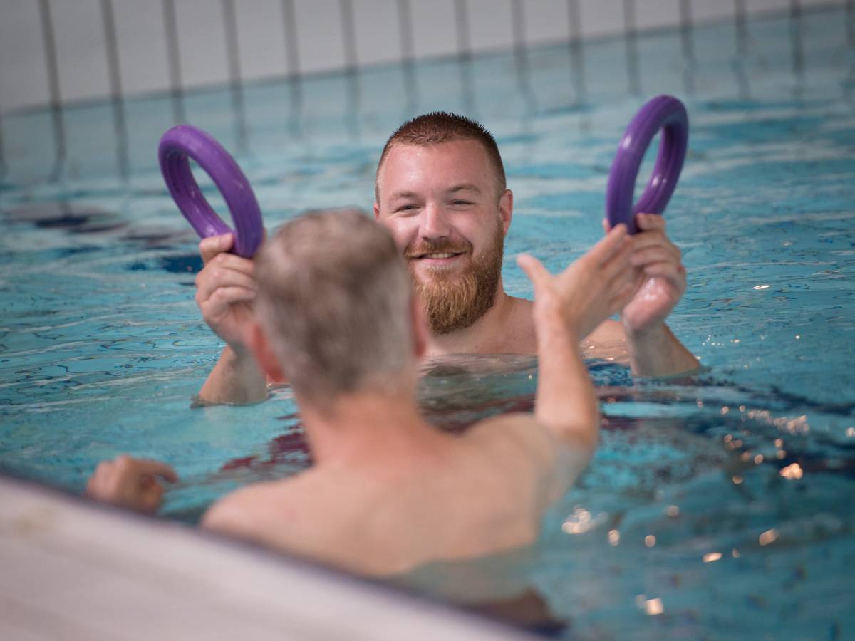 Begeleider en cliënt in zwembad activiteit met paarse ringen